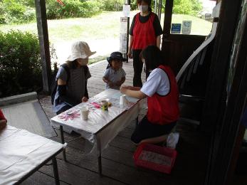 トライやるウィークの生徒が来園者へ紙飛行機の作り方を説明する写真