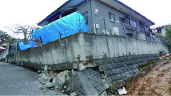 写真：地震の影響で擁壁が崩れ、傾いた家