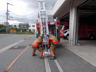訓練で消防車に積んでいる梯子を降ろしている写真