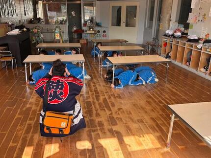 地震発生で机の下にもぐり身を守る園児の写真