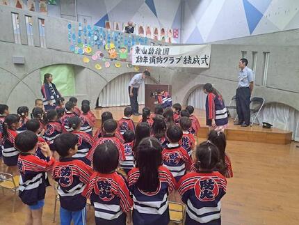 北消防署副署長と幼年消防クラブ員が壇上で対面する様子の写真